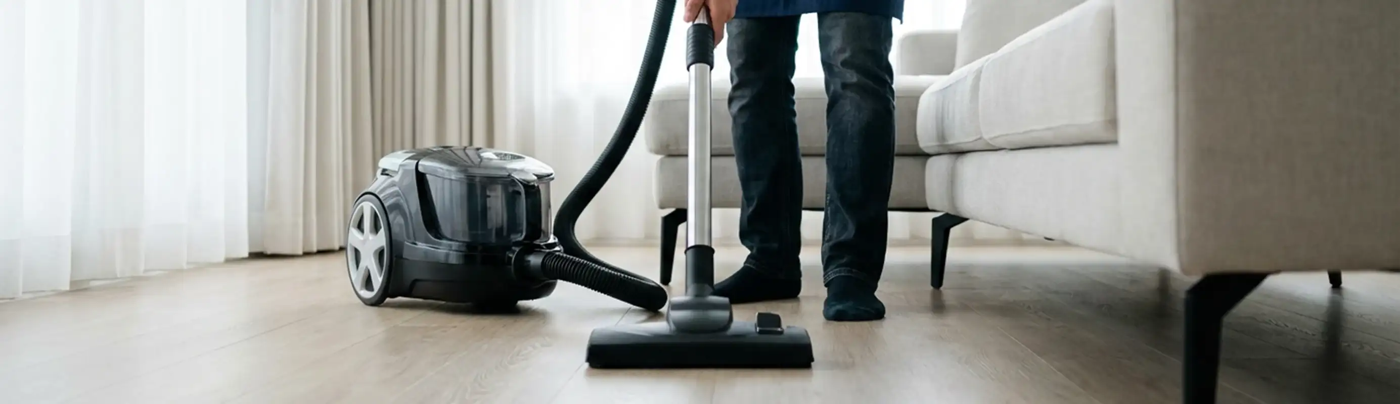 Professional house cleaner vacuuming a living room floor with a canister vacuum cleaner, Tucson, AZ.