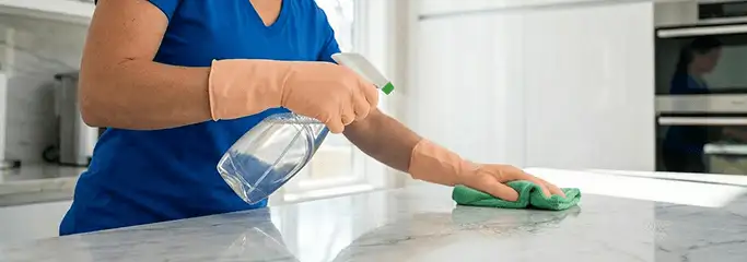 Maid service worker spraying and wiping a kitchen countertop with a microfiber cloth for sanitizing, Tucson, AZ.