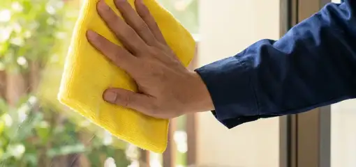 House cleaner wiping a glass window with a yellow microfiber cloth for streak-free cleaning, Tucson, AZ.